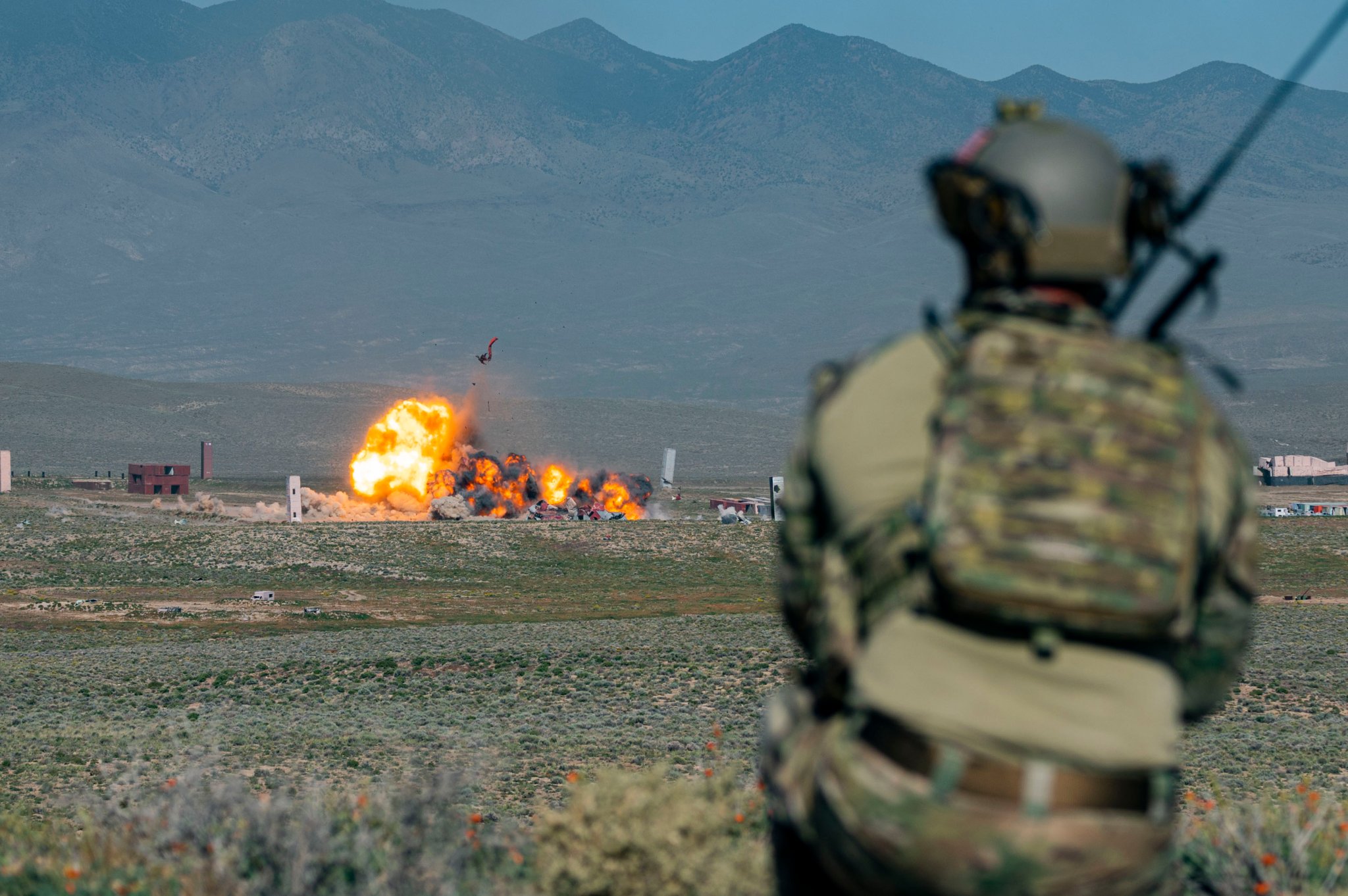 U.S. Air Force Capt. Jason Hoist, Tactical Air Control Party specialist assigned to the 422 Test and Evaluation Squadron, watches as 1K lb. bombs strike a target on the Nevada Test and Training Range, Nevada, Sept. 26, 2023. U.S. Navy FA-18 Super Hornets assigned to Air Test and Evaluation Squadron 9, (VX-9) Naval Air Weapons Station China Lake, California., helped the NTTR conduct target maintenance operations. (U.S. Air Force photo by Senior Airman Zachary Rufus)