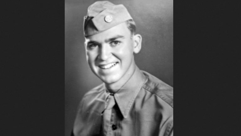 A black and white headshot of a man in an Army uniform smiling.