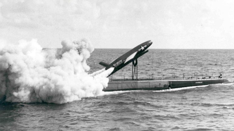 A rocket launches from the top of a submarine, spewing a huge plume of smoke, in a black and white picture.